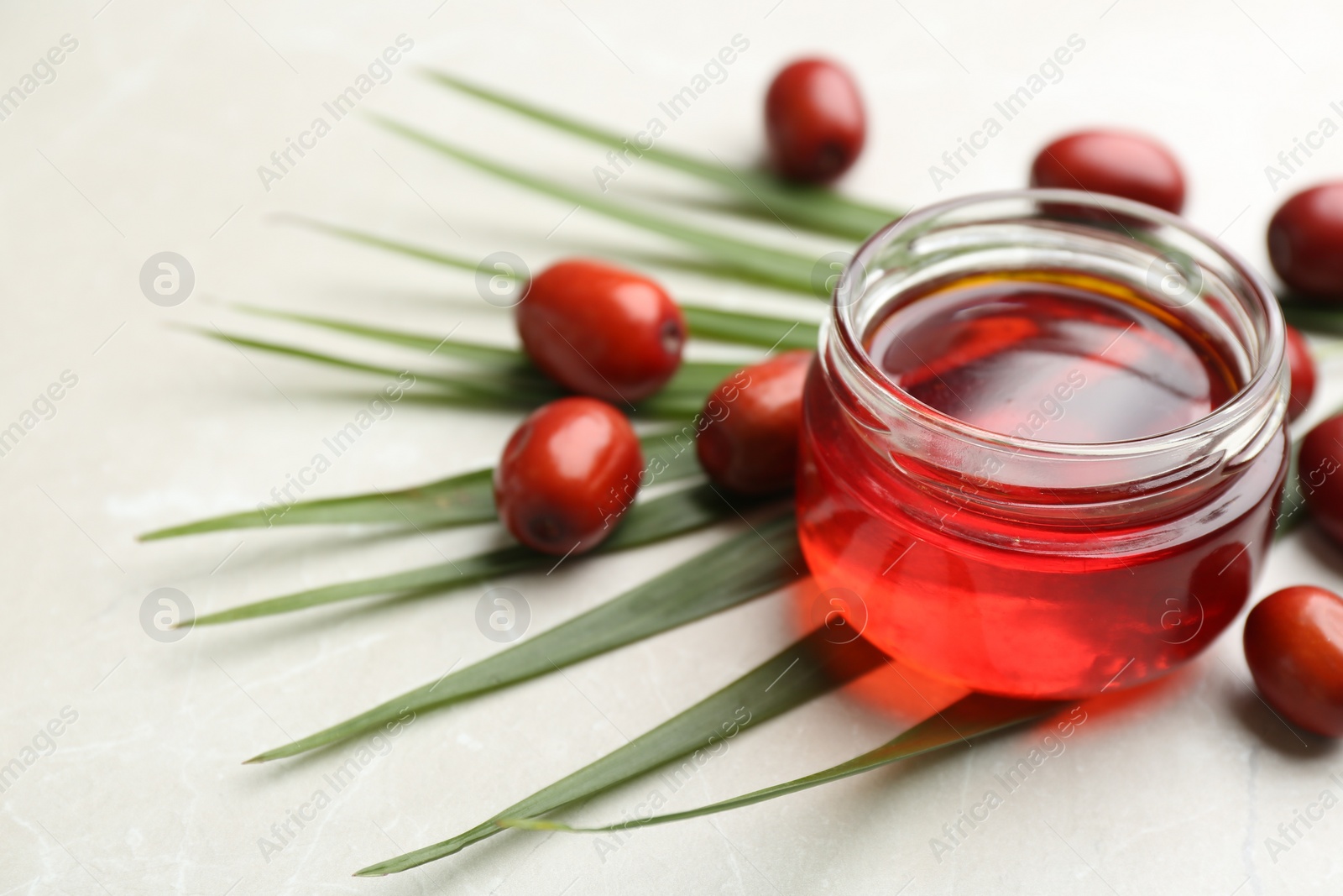 Photo of Palm oil in glass jar, tropical leaf and fruits on light table. Space for text