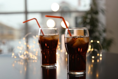 Glasses of cold cola and fairy lights on table