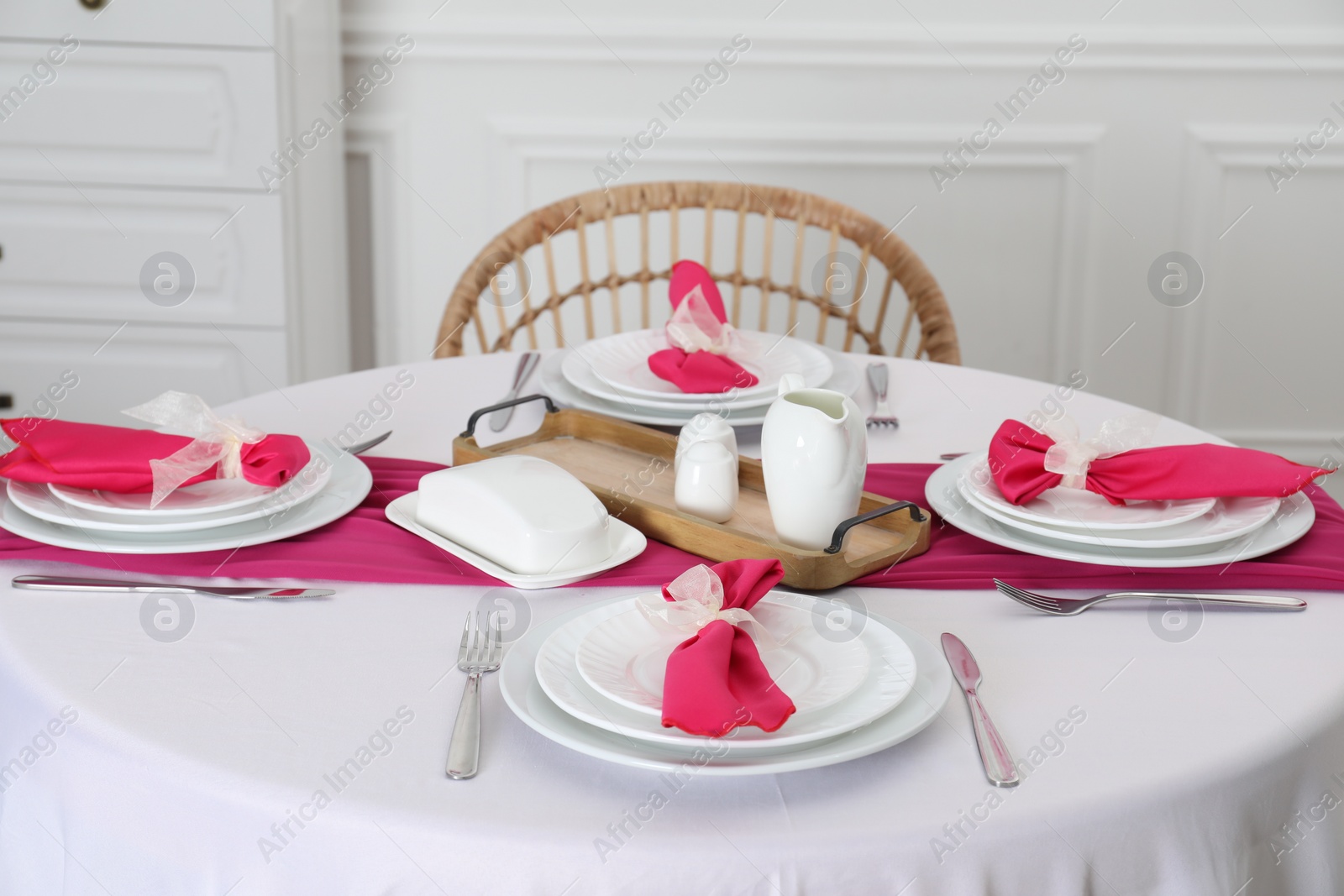 Photo of Color accent table setting. Plates, cutlery and pink napkins in dining room