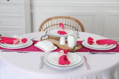Photo of Color accent table setting. Plates, cutlery and pink napkins in dining room