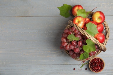 Photo of Wicker basket with fresh fruits and berries on grey wooden table, flat lay. Space for text