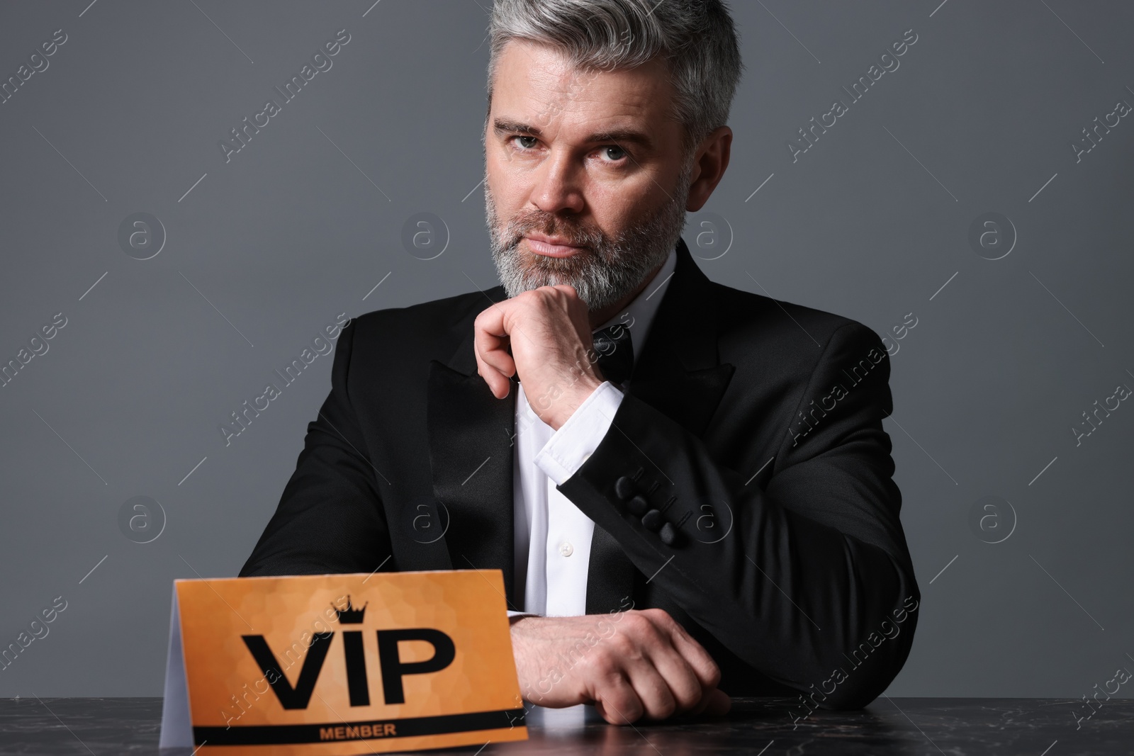 Photo of Handsome man sitting at table with VIP sign on grey background