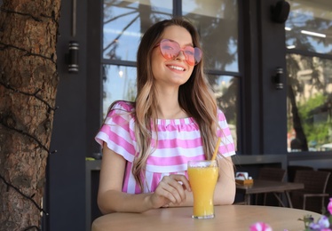 Photo of Happy young woman with heart shaped glasses and juice at cafe
