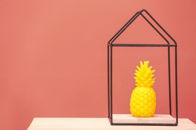 Photo of Stylish pineapple candle on table against color background. Home decorating idea