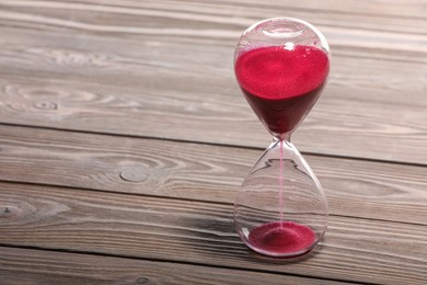 Photo of Hourglass with pink flowing sand on wooden table. Space for text