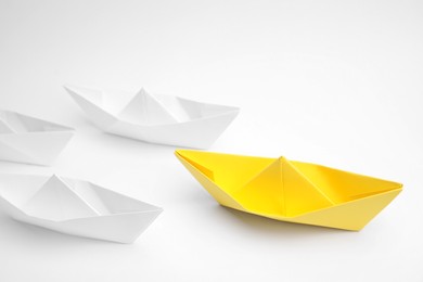 Photo of Group of paper boats following yellow one on white background, above view. Leadership concept