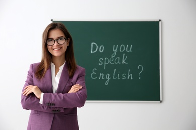 Photo of Teacher near green chalkboard with words Do You Speak English?