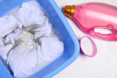 Photo of Basin with clothes and detergents on white surface, flat lay. Hand washing laundry