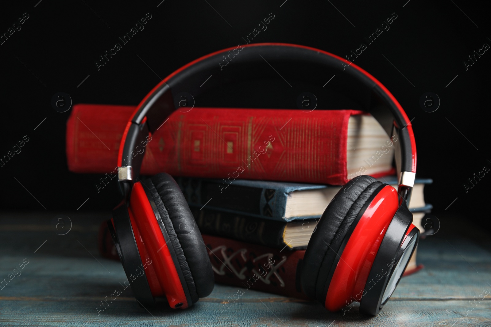 Photo of Headphones and stack of books on light blue wooden table, closeup