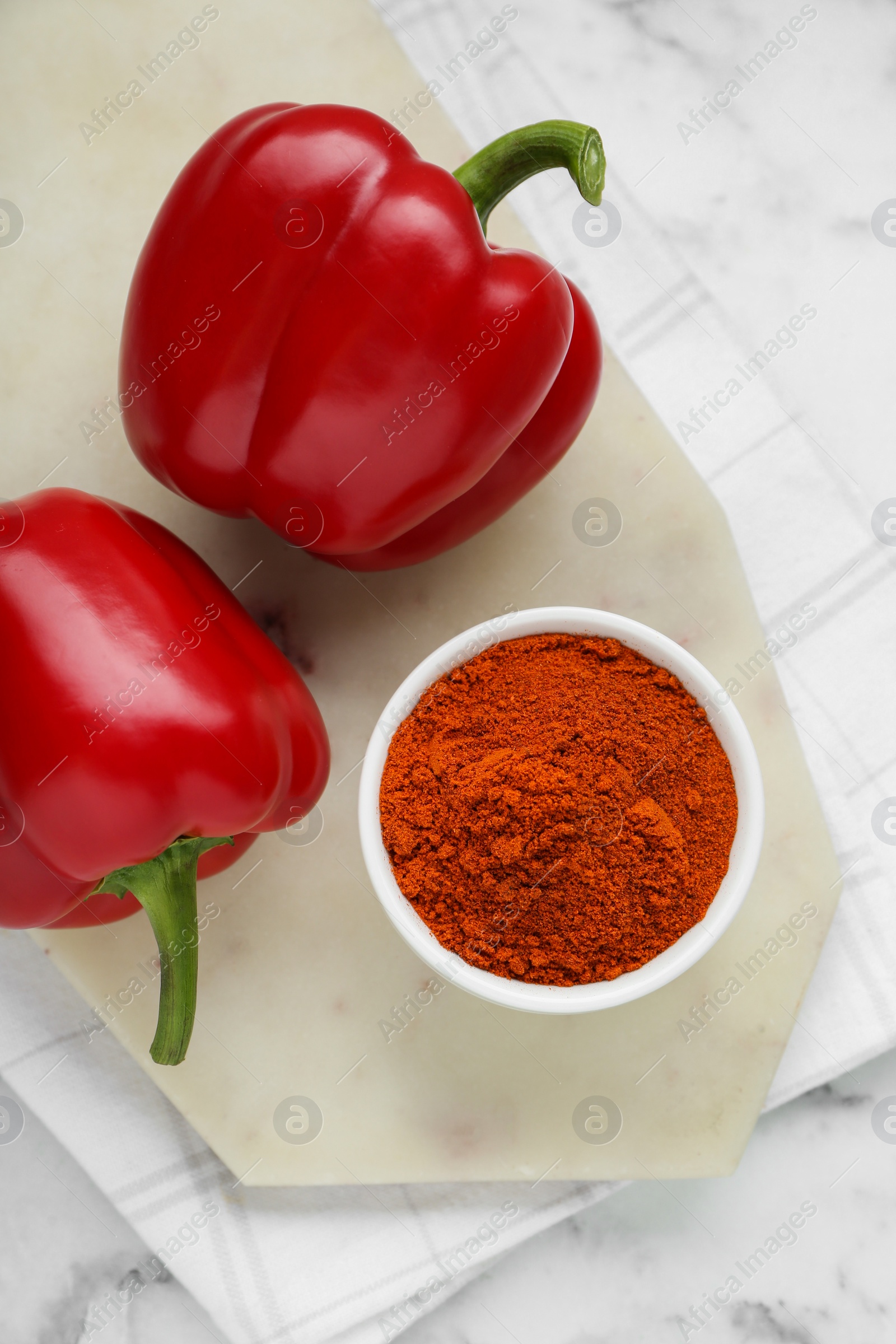 Photo of Bowl with aromatic paprika powder and fresh bell peppers on white marble table, flat lay