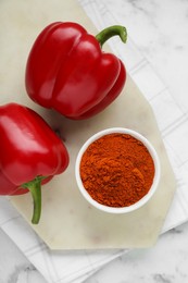 Photo of Bowl with aromatic paprika powder and fresh bell peppers on white marble table, flat lay