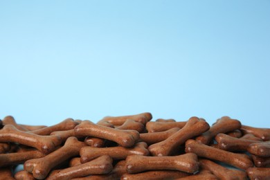 Photo of Bone shaped dog cookies on light blue background, closeup. Space for text