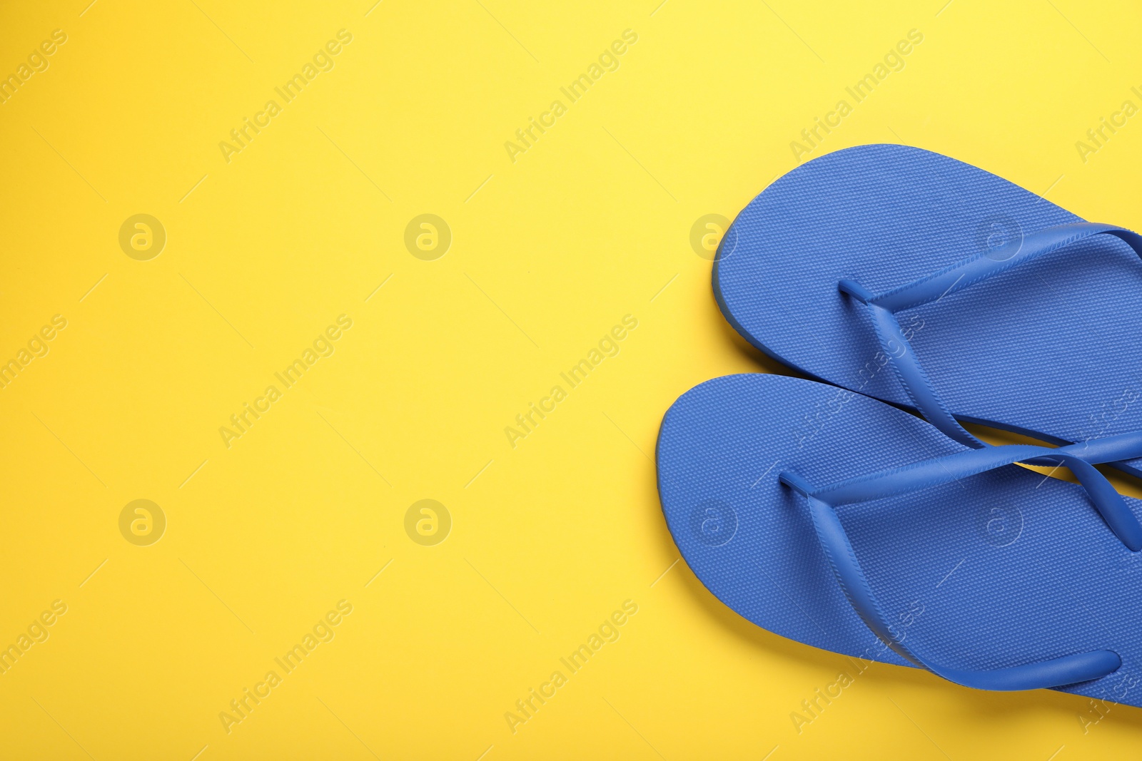 Photo of Stylish blue flip flops on yellow background, top view. Space for text