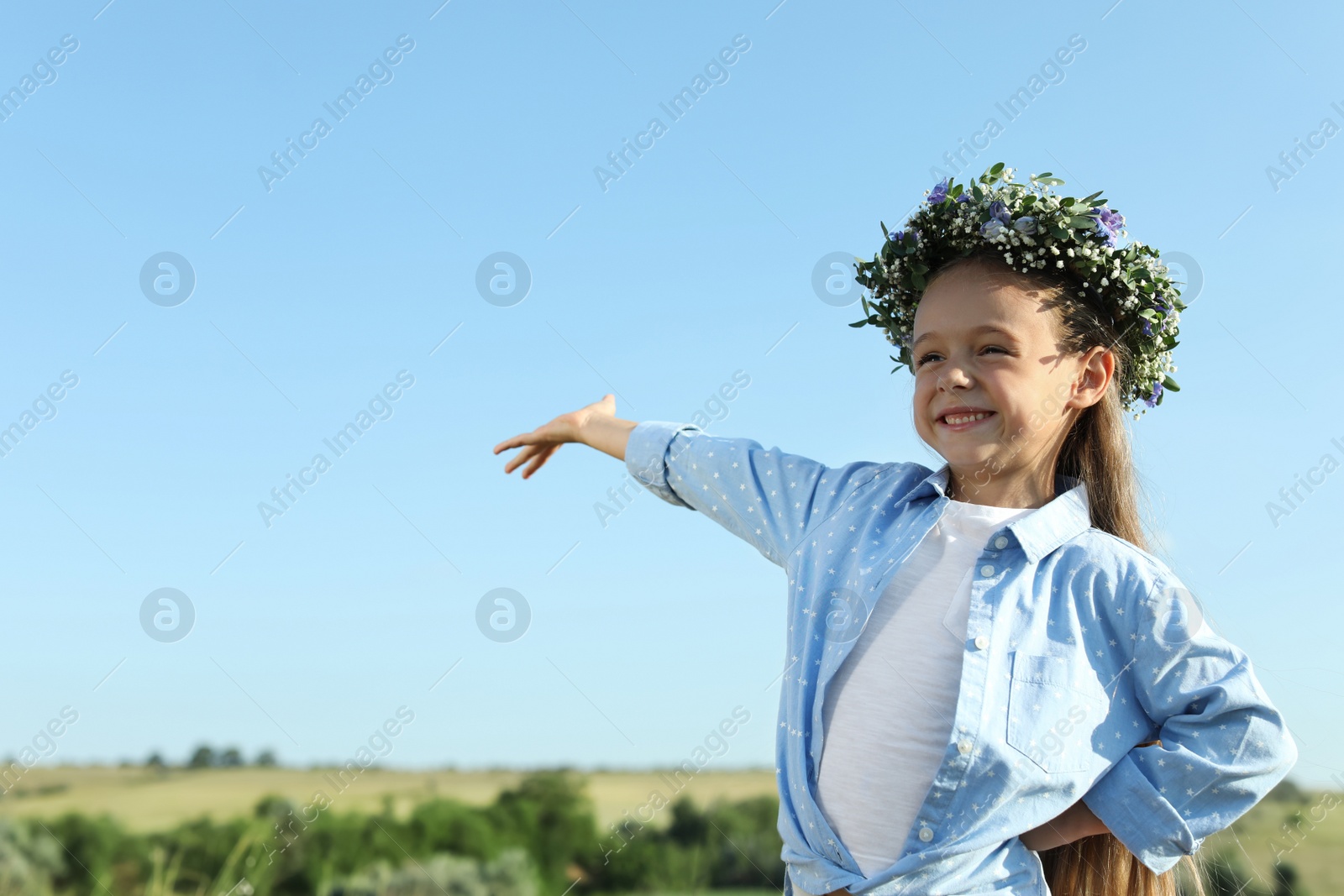 Photo of Cute little girl wearing flower wreath outdoors, space for text. Child spending time in nature