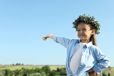 Photo of Cute little girl wearing flower wreath outdoors, space for text. Child spending time in nature