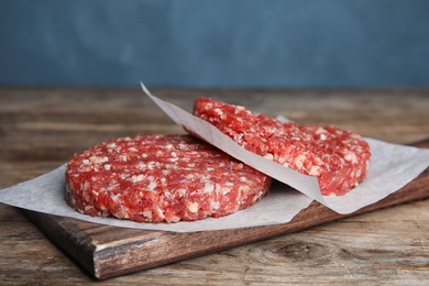 Photo of Raw meat cutlets for burger on wooden table against blue background