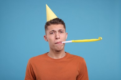 Young man in party hat with blower on light blue background