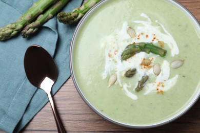 Photo of Delicious asparagus soup with pumpkin seeds served on wooden table, flat lay