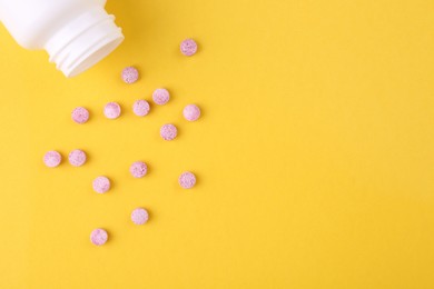 Photo of Bottle and vitamin pills on yellow background, top view. Space for text