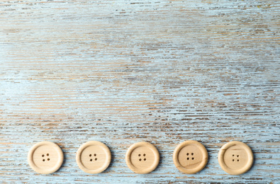 Many sewing buttons on light wooden background, flat lay. Space for text