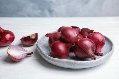 Plate with ripe red onions on table