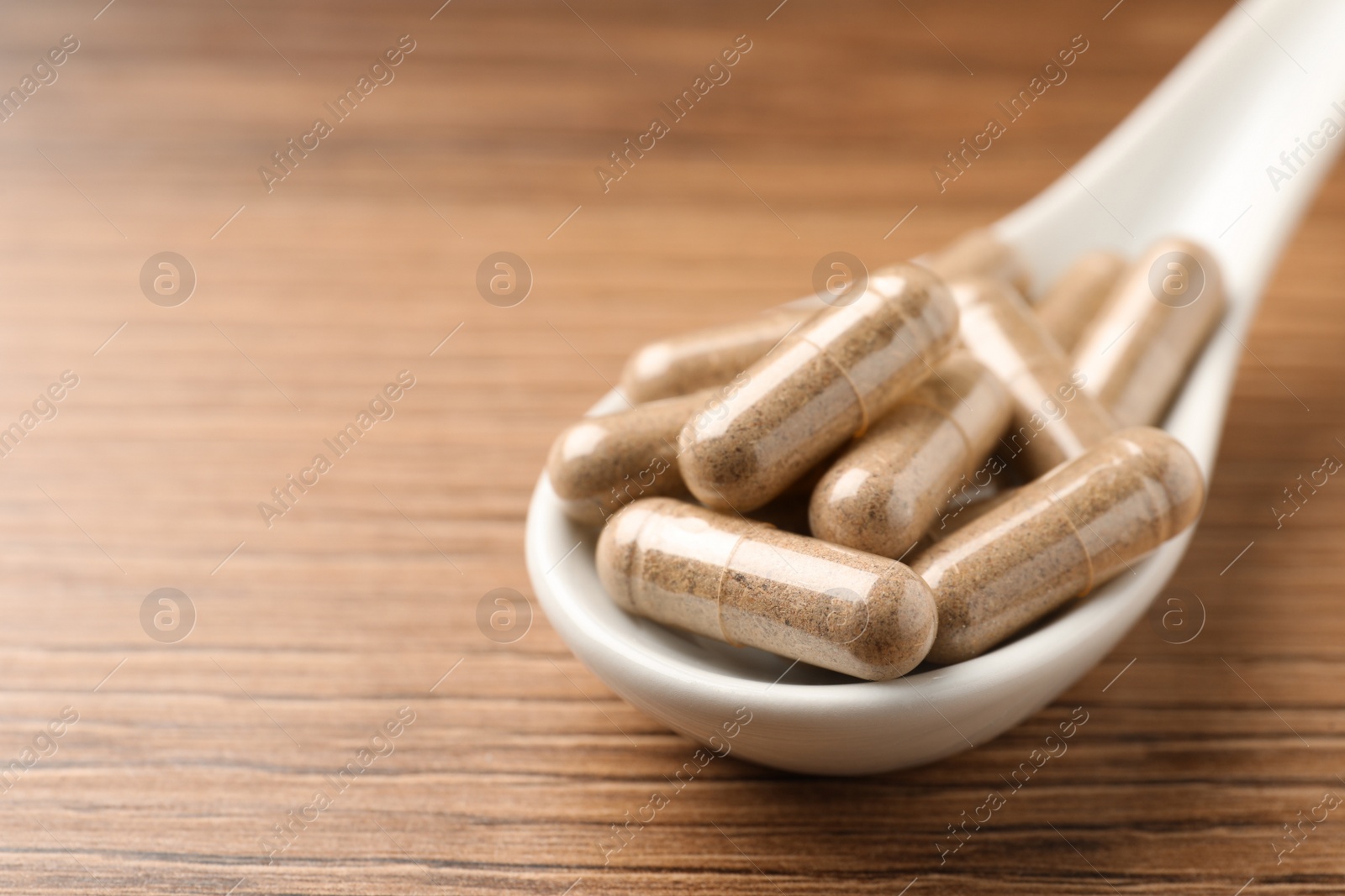 Photo of Spoon with dietary supplement capsules on wooden table, closeup. Space for text