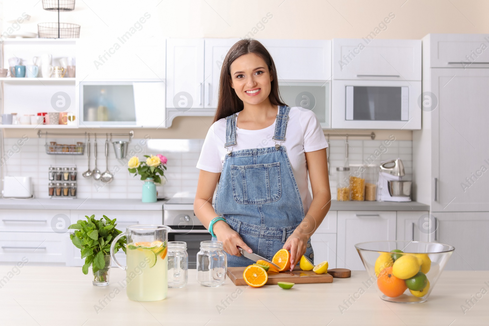 Photo of Young woman preparing lemonade on table in kitchen. Natural detox drink