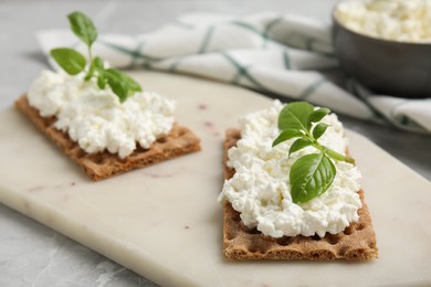 Photo of Crispy crackers with cottage cheese and basil on light grey marble table, closeup