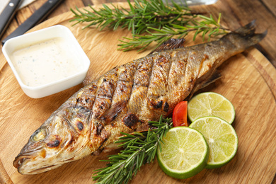 Photo of Delicious grilled fish with lime on wooden board, closeup