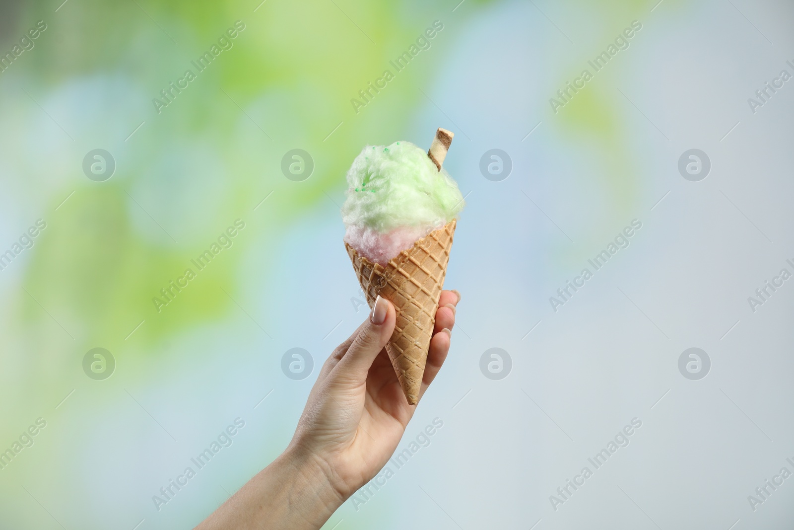 Photo of Woman holding waffle cone with cotton candy on blurred background, closeup