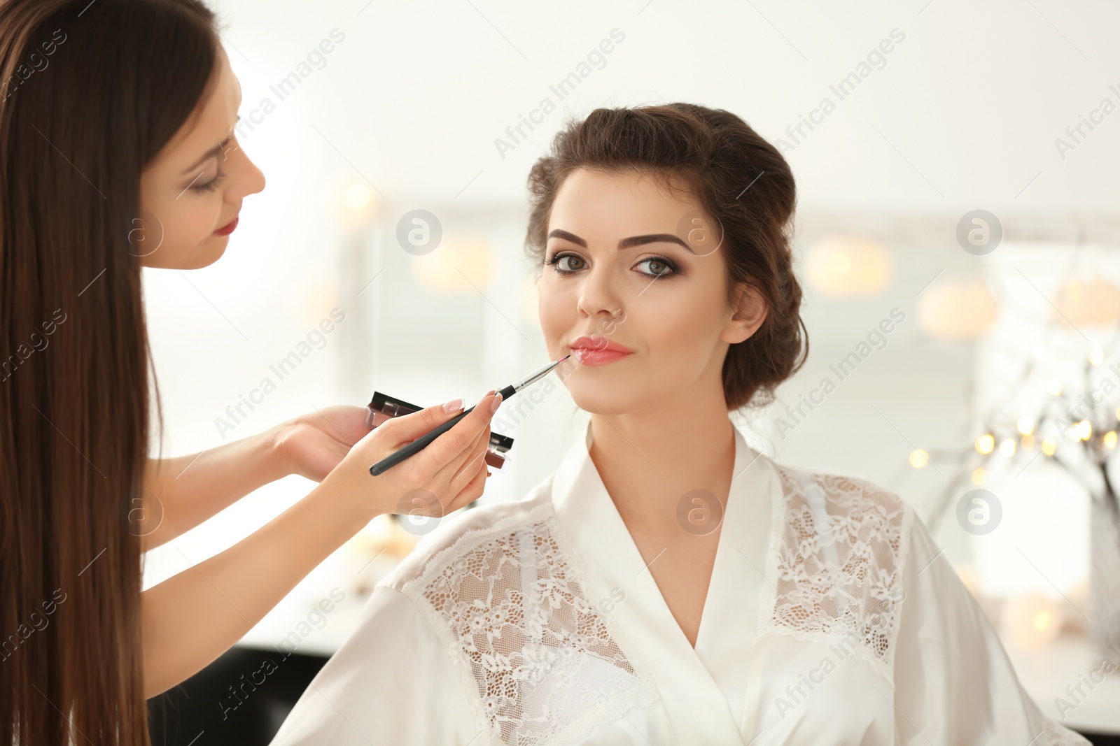 Photo of Makeup artist preparing bride before her wedding in room