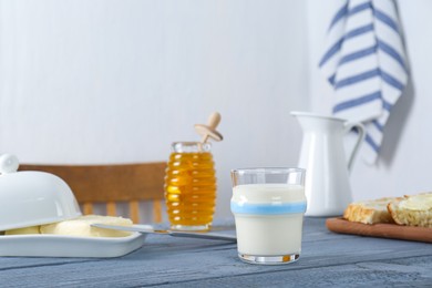 Photo of Glass with milk, honey, bread and butter on grey wooden table