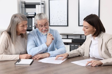 Elderly couple consulting insurance agent about pension plan at wooden table indoors