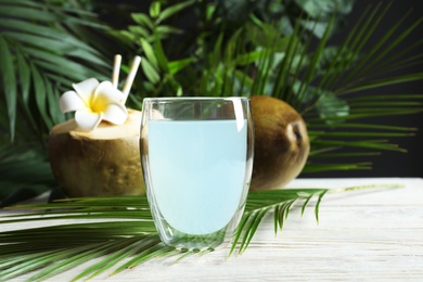 Glass of fresh coconut water and tropical palm leaf on wooden table