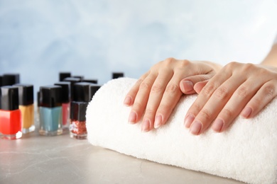 Photo of Young woman waiting for manicure near bottles of nail polish at table in salon, closeup. Space for text