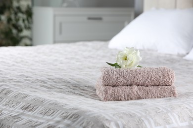 Photo of Stack of clean towels and Eustoma flower on bed indoors, space for text