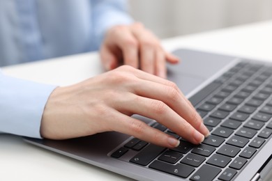 Photo of E-learning. Woman using laptop at white table indoors, closeup