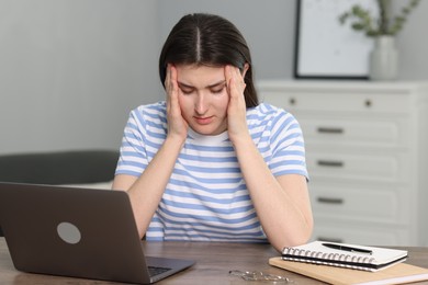 Photo of Overwhelmed woman sitting with laptop at table indoors