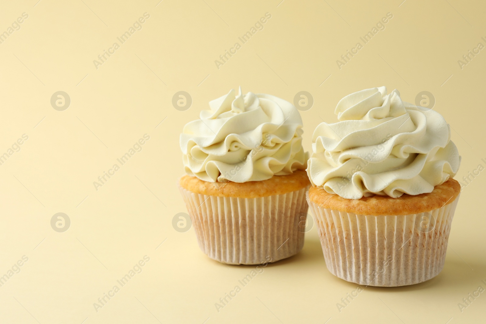 Photo of Tasty vanilla cupcakes with cream on pale yellow background, space for text