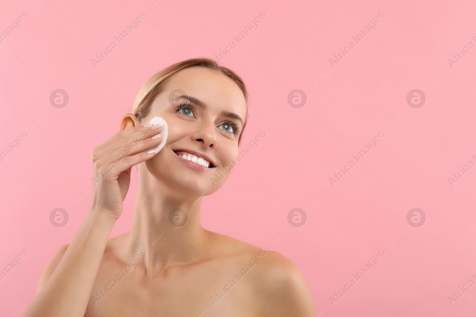 Photo of Smiling woman removing makeup with cotton pad on pink background. Space for text