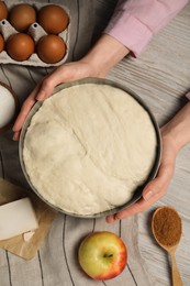 Woman holding bowl with fresh yeast dough and ingredients for cake on wooden table, closeup