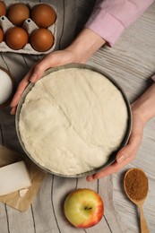 Photo of Woman holding bowl with fresh yeast dough and ingredients for cake on wooden table, closeup