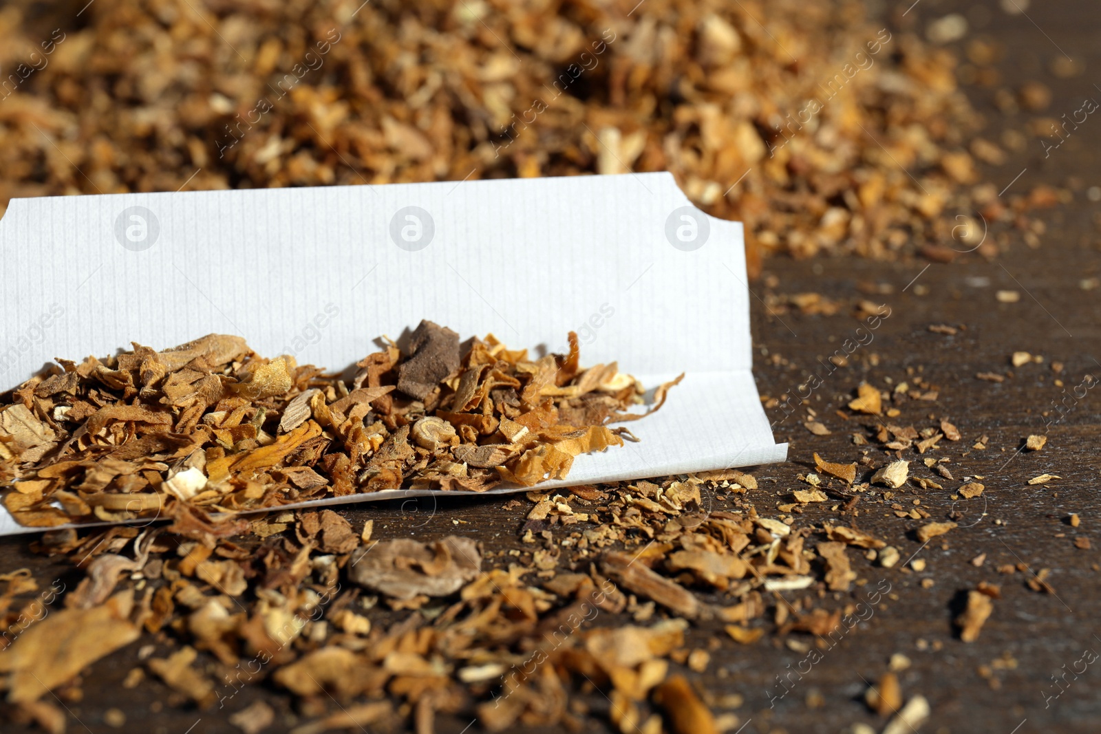 Photo of Paper and tobacco on wooden table, closeup. Making hand rolled cigarette