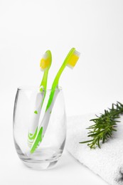 Light green toothbrushes in glass holder, terry towel and rosemary on white background