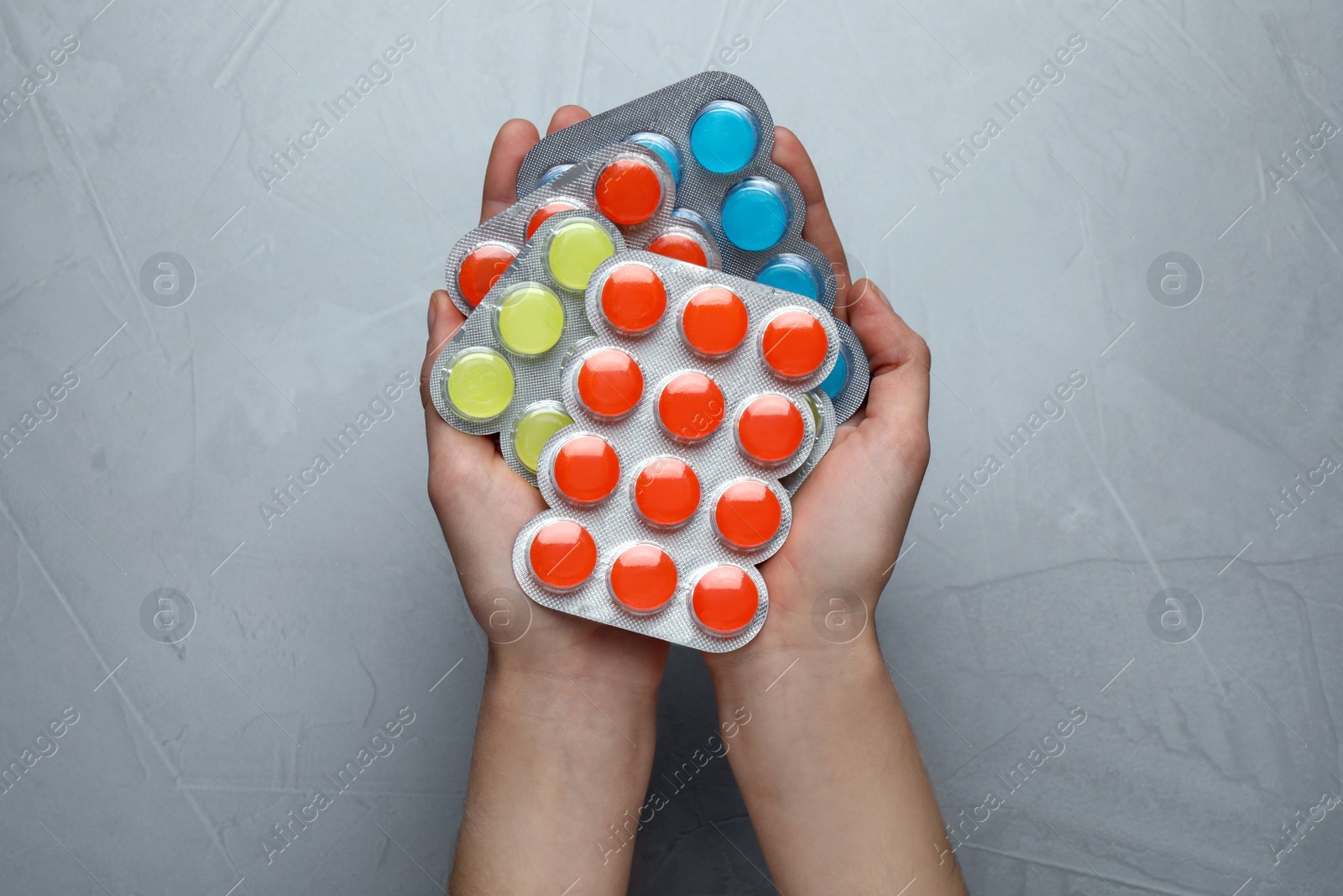 Photo of Woman holding blisters with cough drops on grey background, top view