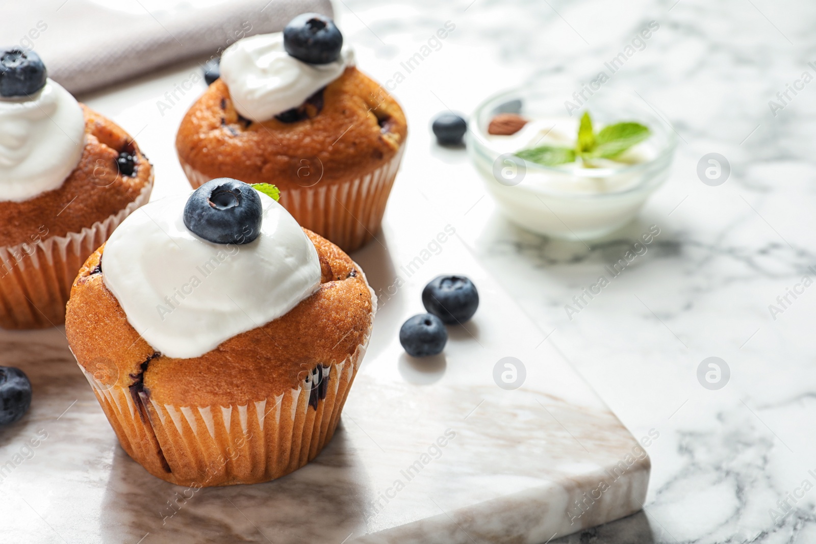 Photo of Marble board with tasty muffins, cream and blueberries on table