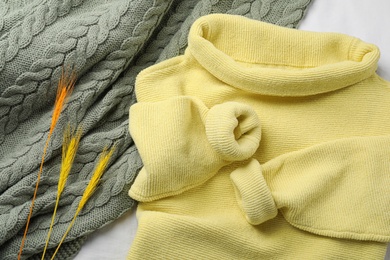 Photo of Beautiful yellow warm sweater, plaid and decorative spikes on white bedsheet, flat lay