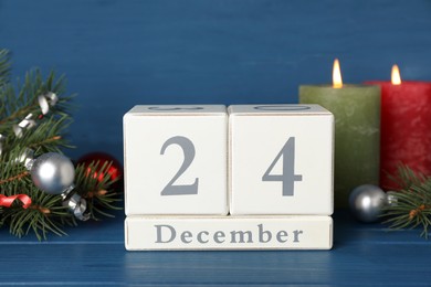 Photo of December 24 - Christmas Eve. Wooden block calendar and festive decor on blue table