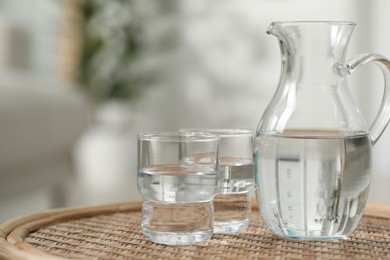 Jug and glasses with clear water on wicker surface against blurred background, closeup. Space for text