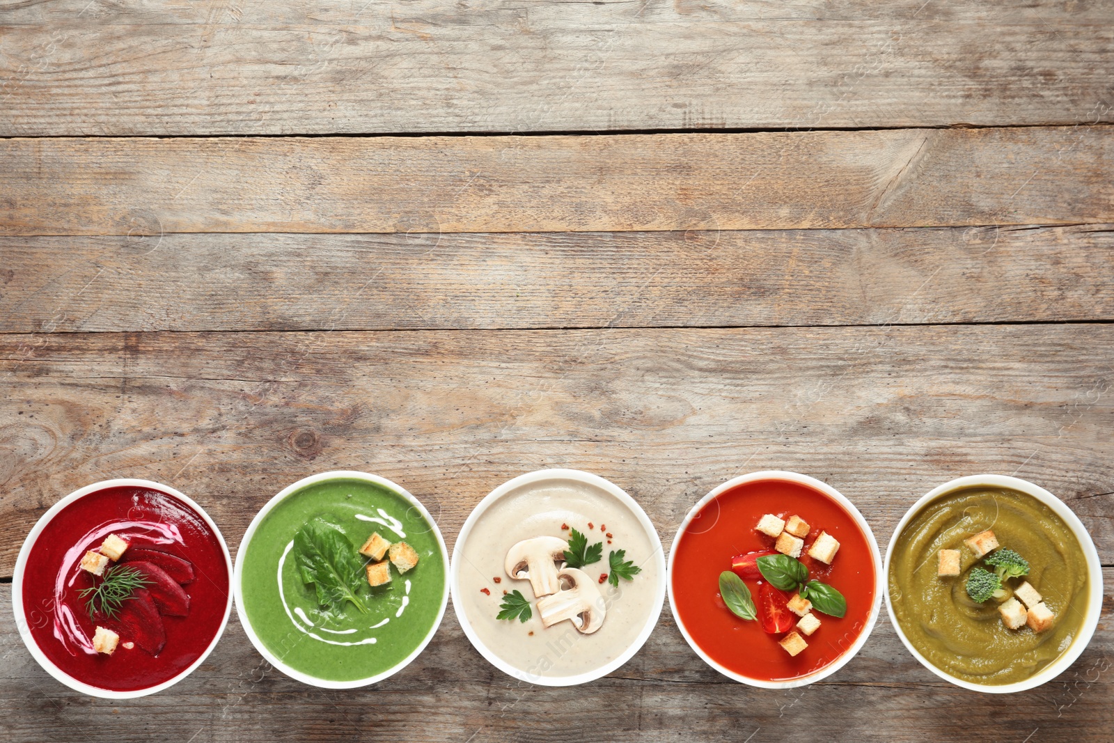 Photo of Various cream soups in bowls and space for text on wooden background, top view